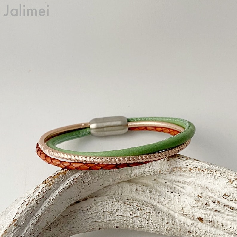 May include: A multi-strand bracelet featuring a braided brown leather band, a light green band, and a rose gold band. The bracelet has a magnetic clasp. The word "Jalimei" is in the upper left corner.