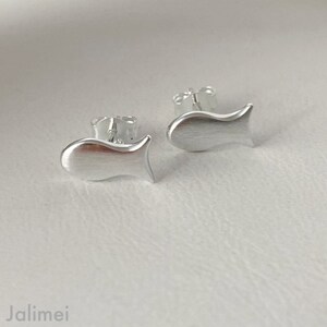 K&ouml;nnte beinhalten: Ein Paar silberne Ohrstecker in Fischform. Die Ohrringe sind klein und zart, mit einer geb&uuml;rsteten Oberfl&auml;che.