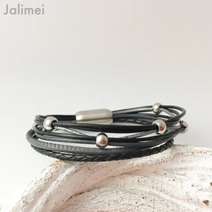 Puede incluir: Un brazalete de cuero negro con una correa de cuero trenzada y cuentas de metal plateado. El brazalete tiene un cierre magn&eacute;tico.