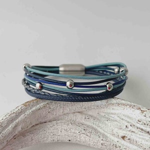 May include: A multi-strand leather bracelet with a magnetic clasp. The bracelet is made of blue and gray leather and features silver beads.