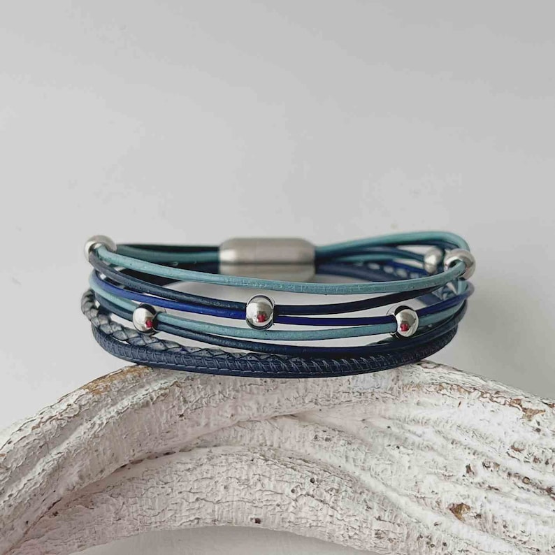 May include: A multi-strand leather bracelet with a magnetic clasp. The bracelet is made of blue and gray leather and features silver beads.