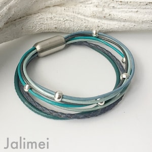 May include: Multi-strand leather bracelet with a silver clasp and silver beads. The bracelet is made of teal, blue, and gray leather.