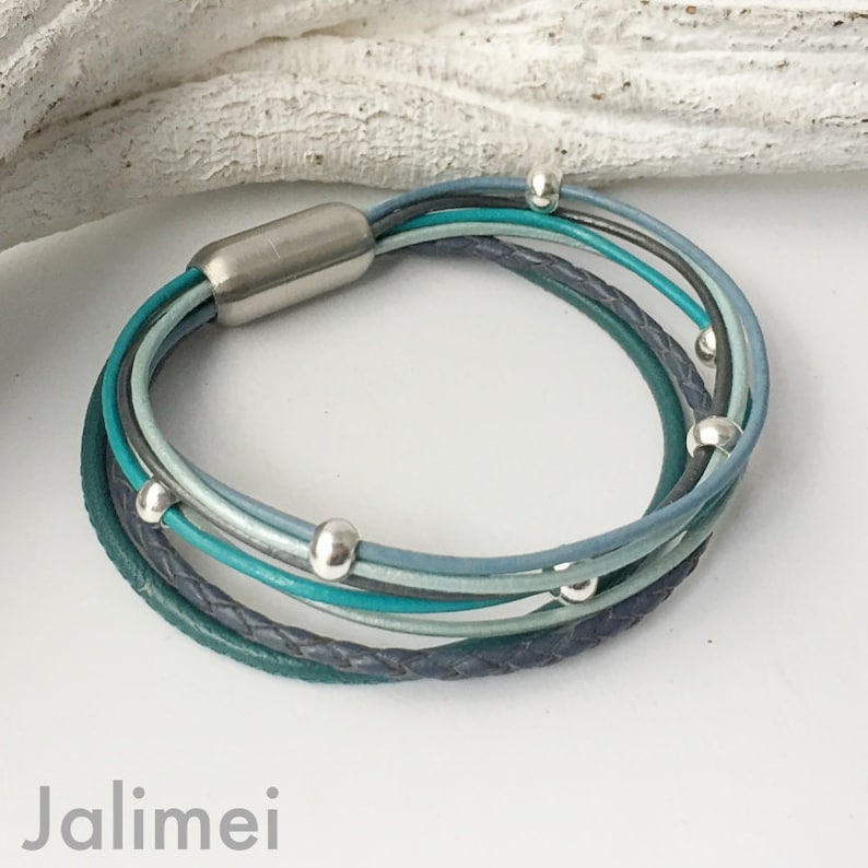 May include: Multi-strand leather bracelet with a silver clasp and silver beads. The bracelet is made of teal, blue, and gray leather.