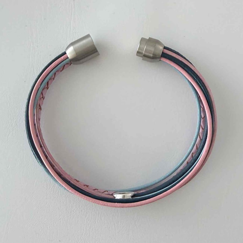 May include: A multi-strand bracelet with a magnetic clasp. The bracelet features pink, light blue, and dark blue leather strands. The clasp is made of silver-coloured metal.