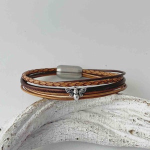 May include: A multi-strand leather bracelet with a silver bee charm. The bracelet is made of brown and tan leather and has a magnetic clasp.