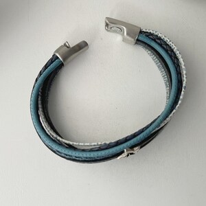 K&ouml;nnte beinhalten: Ein mehrlagiges Lederarmband mit einem silbernen Verschluss. Das Armband besteht aus blauem, schwarzem und wei&szlig;em Leder.