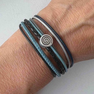 May include: A layered leather bracelet with a silver spiral charm. The bracelet features black, blue, and gray leather straps.