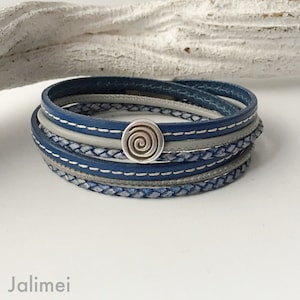 May include: A multi-layered leather bracelet with a silver spiral charm. The bracelet is made of blue and grey leather and has a braided design.