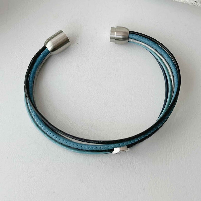 May include: A multi-strand leather bracelet with a silver magnetic clasp. The bracelet features blue and black leather strands.
