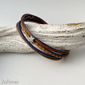 May include: A multi-layered leather bracelet with a silver star charm. The bracelet is made of brown and blue leather and is braided together.