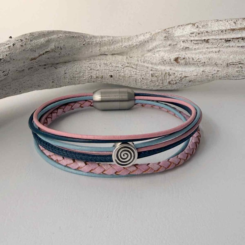 May include: A multi-strand bracelet with pink, light blue, and navy blue leather cords. It has a silver-coloured magnetic clasp and a decorative silver-coloured charm with a spiral design. The bracelet is a stylish accessory.