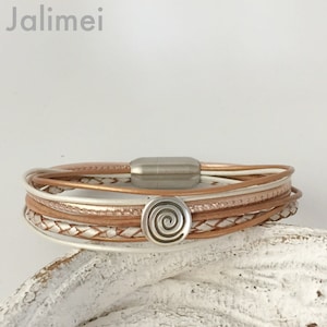 Könnte beinhalten: Ein mehrreihiges Lederarmband mit einem silbernen Spiral-Anhänger. Das Armband besteht aus weißem und roségoldem Leder und hat einen Magnetverschluss.
