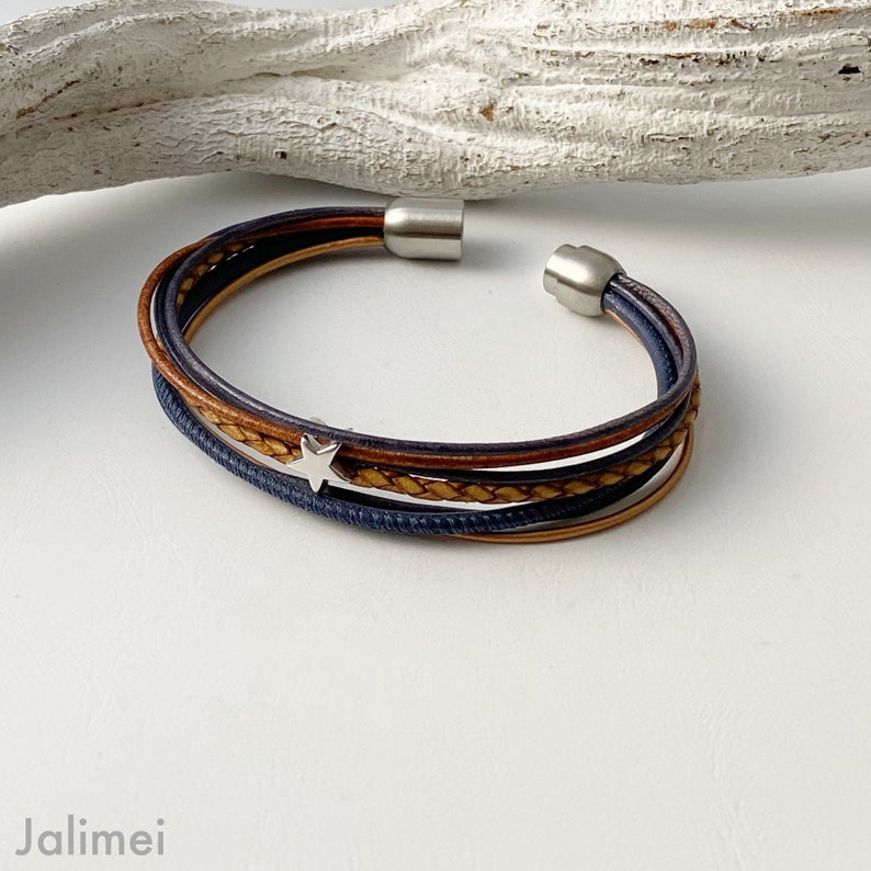 May include: A multi-strand leather bracelet with a silver star charm. The bracelet is made of brown and blue leather and has a silver clasp.