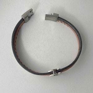 May include: A brown leather bracelet with silver metal clasps. The bracelet is made of two pieces of leather that are stitched together.