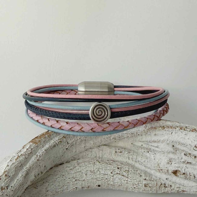 May include: A multi-strand bracelet with pink, blue, and black leather cords. The bracelet has a silver magnetic clasp and a spiral charm. The braided leather adds texture to the design.