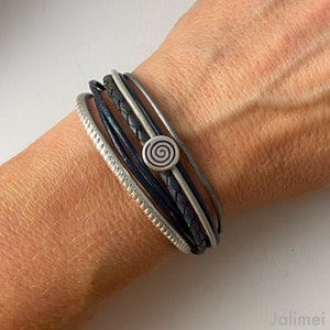 Könnte beinhalten: Ein mehrlagiges Armband mit einem silbernen Spiral-Anhänger. Das Armband besteht aus schwarzen und grauen Lederbändern.