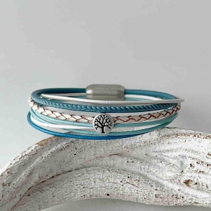 May include: A multi-layered bracelet with a silver tree of life charm. The bracelet features shades of blue and white leather straps.