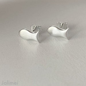 K&ouml;nnte beinhalten: Ein Paar silberne Ohrstecker in Fischform. Die Ohrringe sind klein und zart, mit einer geb&uuml;rsteten Oberfl&auml;che.