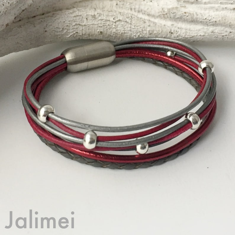 May include: A multi-strand leather bracelet with a magnetic clasp. The bracelet is made of red and gray leather and features silver beads.