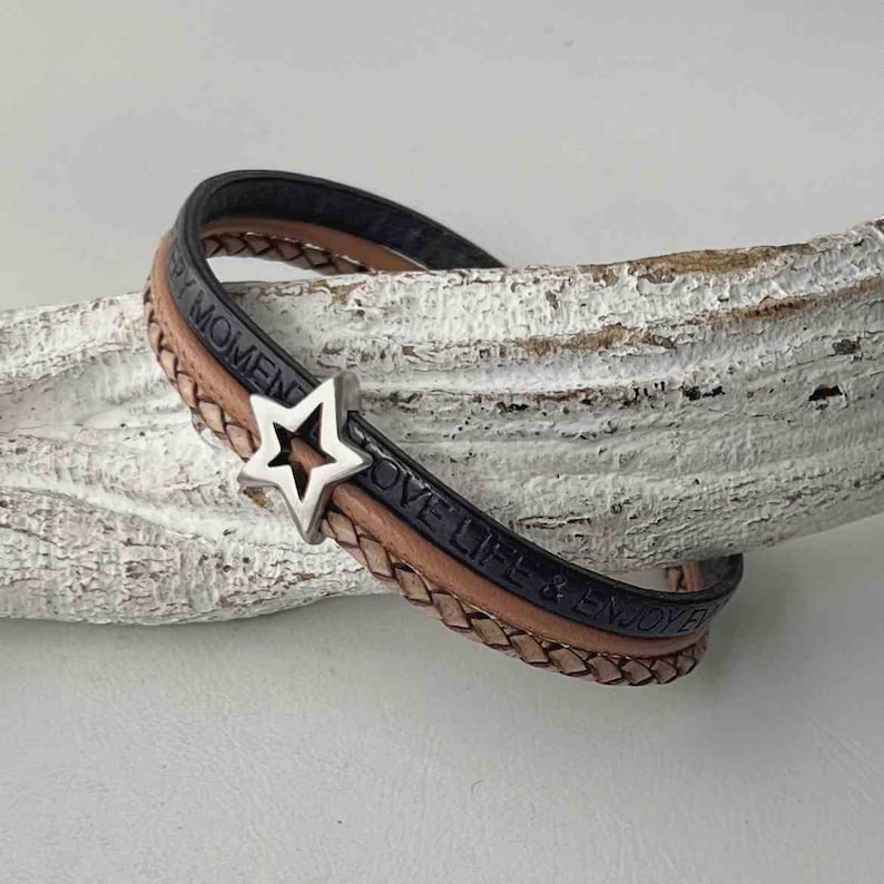 May include: A triple-wrap leather bracelet with a silver star charm. The bracelet is made of black, brown, and tan leather and has the words "Love Life & Enjoy Every Moment" embossed on it.