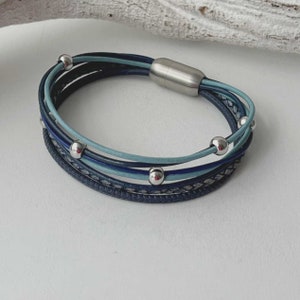 May include: A multi-strand leather bracelet with a silver magnetic clasp. The bracelet features blue and light blue leather strands with silver beads.
