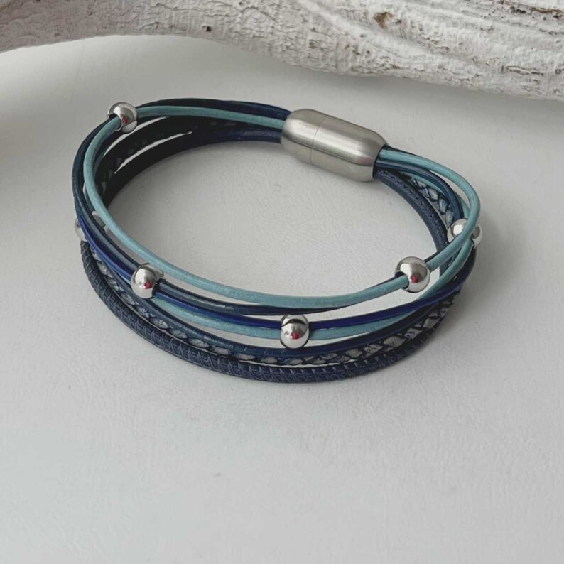 May include: A multi-strand leather bracelet with a silver magnetic clasp. The bracelet features blue and light blue leather strands with silver beads.