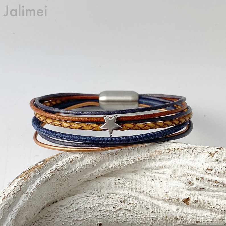 May include: A multi-layered leather bracelet with a silver star charm. The bracelet is made of brown and blue leather and has a magnetic clasp.