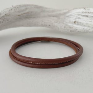 以下が含まれることがあります： 二重巻きのデザインの茶色の革製ブレスレット。ブレスレットは暖かく豊かな茶色で、高品質の革で作られているようです。デザインはシンプルでエレガントで、日常使いに適しています。