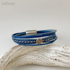 May include: A multi-strand leather bracelet with a magnetic clasp. The bracelet is made of blue and white leather and features a small silver charm with a gold spiral design.