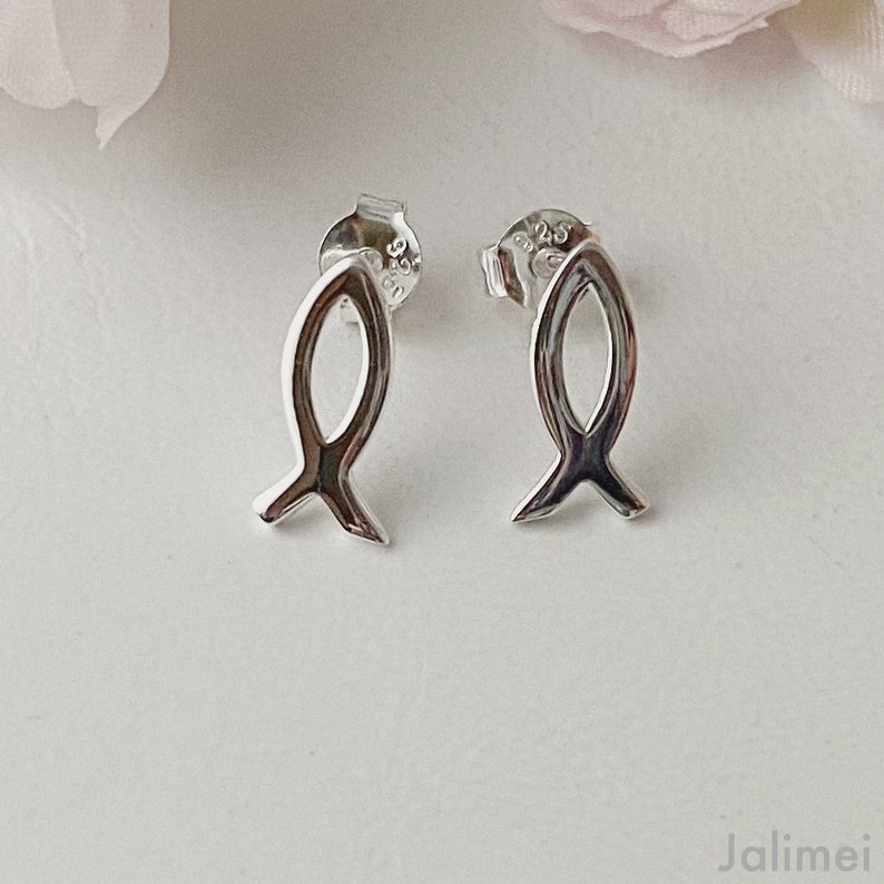 May include: A pair of silver fish-shaped stud earrings. The earrings are small and delicate, and they have a simple, elegant design.
