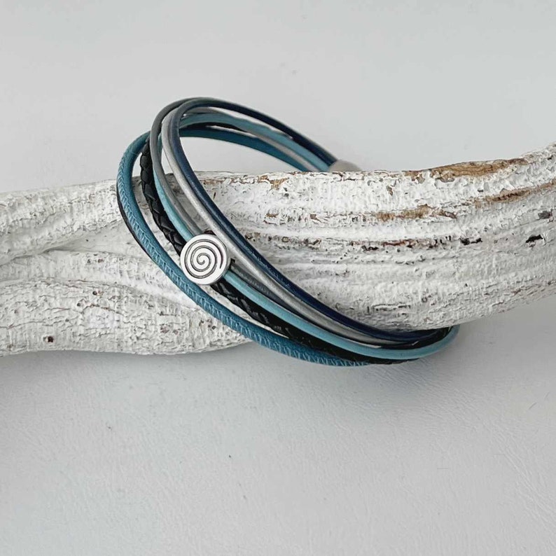 May include: A multi-strand leather bracelet with a silver spiral charm. The bracelet is made of blue, black, and gray leather cords.