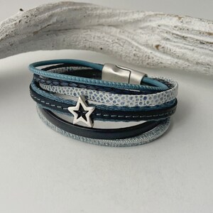 K&ouml;nnte beinhalten: Ein mehrlagiges Armband mit einem silbernen Sternanh&auml;nger. Das Armband besteht aus blauem und schwarzem Leder und hat einen magnetischen Verschluss.