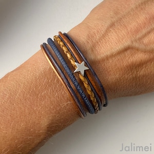 May include: A multi-layered leather bracelet with a silver star charm. The bracelet features a combination of brown and blue leather straps.