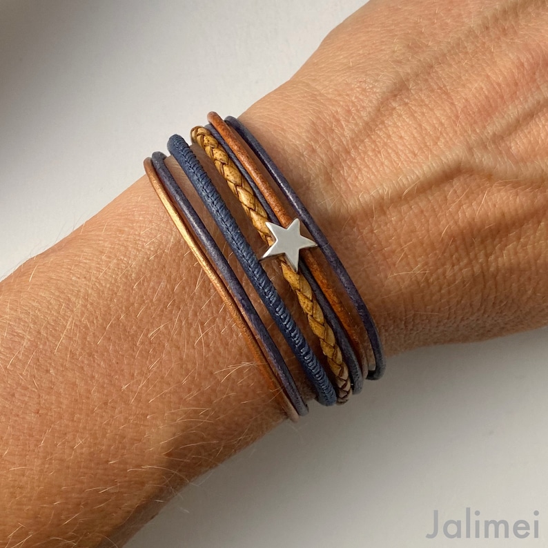 May include: A multi-layered leather bracelet with a silver star charm. The bracelet features a combination of brown and blue leather straps.