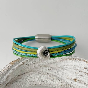 Può includere: Braccialetto in pelle multifilo con ciondolo a forma di conchiglia argentata. Il braccialetto presenta fili di pelle turchese, verde e giallo.