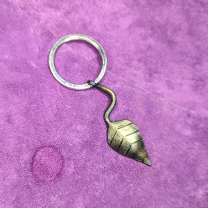 May include: A silver key ring with a black metal leaf charm. The leaf is textured and has a gold finish.