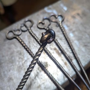 May include: Five twisted metal skewers with heart-shaped handles. The skewers are made of a dark metal and have a rustic finish.