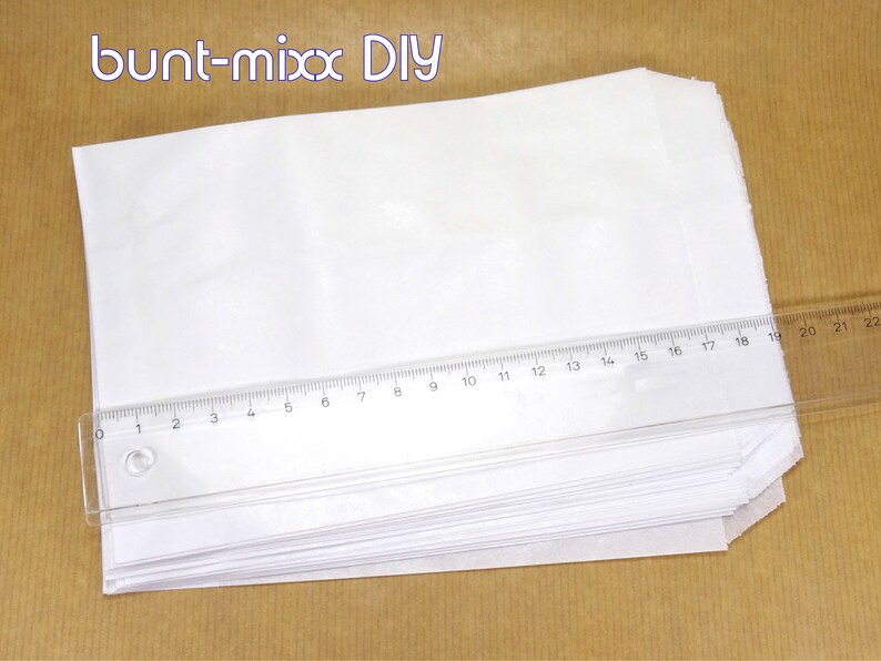 K&ouml;nnte beinhalten: Ein Stapel wei&szlig;er Papiert&uuml;ten mit einem Lineal darauf. Das Lineal ist in Zoll und Zentimetern gekennzeichnet. Die Papiert&uuml;ten sind gefaltet und einsatzbereit.