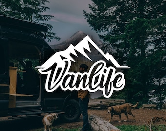 May include: A black van parked in a forest setting with a white mountain range graphic that says "Vanlife" in black lettering. A person is standing next to the van and two dogs are in the foreground.