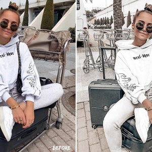 Peut inclure: Une femme portant un sweat-shirt blanc avec le texte "west-bye" et des lunettes de soleil noires est assise sur une valise &agrave; l'a&eacute;roport.