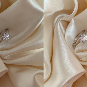 May include: A close-up of a silver ring with a large, clear diamond on a white satin background. The diamond sparkles brightly in the light.
