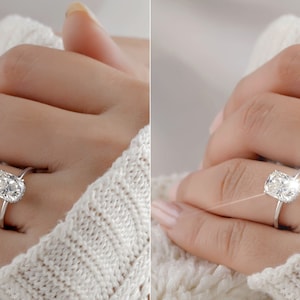 May include: A close-up of a hand wearing a silver ring with a large, oval-shaped diamond. The diamond is sparkling brightly, and the ring is set on a thin band.