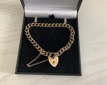 May include: Gold-toned chain bracelet with a heart-shaped padlock clasp. The bracelet is displayed in a black jewelry box with a white interior. The chain links are thick and the padlock has a keyhole detail.