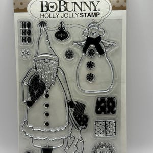 May include: A set of 10 clear rubber stamps featuring a snowman, a gnome, a wreath, presents, and the words "HO HO HO" and "JOY". The stamps are packaged on a brown card with the text "BOBUNNY HOLLY JOLLY STAMP" printed on it.