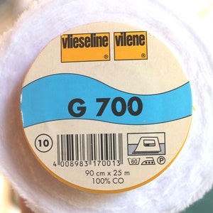 Könnte beinhalten: Eine weiße Rolle Vlieseline Vilene G 700 Einlage, ein verschweißbares Gewebe, das zur Stabilisierung und Verstärkung von Stoffen verwendet wird. Das Etikett ist gelb und blau mit dem Text "Vlieseline Vilene G 700" und einem Barcode. Das Etikett enthält auch Anweisungen zum Waschen und Bügeln.