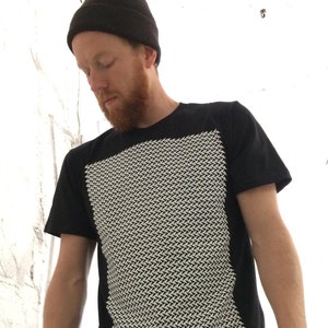 May include: A black t-shirt with a white geometric pattern on the front. The pattern is made up of small, angled lines that create a textured effect.