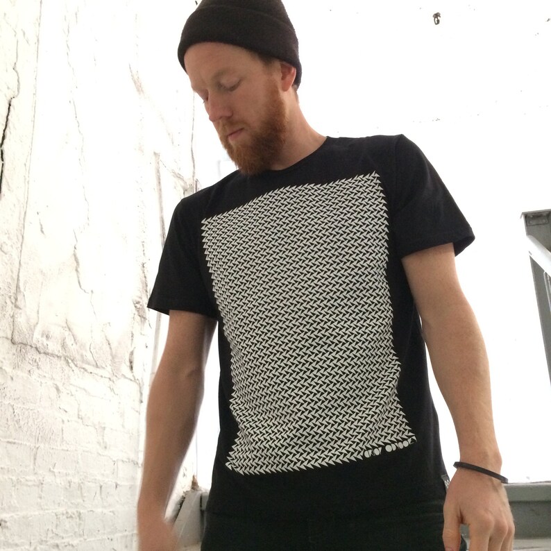 May include: A black t-shirt with a white geometric pattern on the front. The pattern is made up of small, angled lines that create a textured effect.