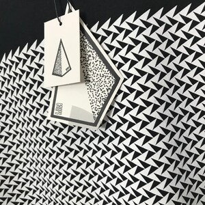 May include: Black and white graphic t-shirt with a geometric pattern of white triangles on a black background. The shirt has a white tag with the word "CARGO" printed on it.