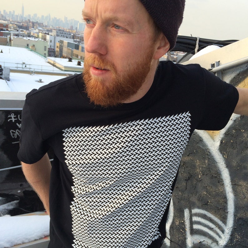 May include: A black t-shirt with a white geometric pattern. The pattern is made up of small triangles that are arranged in a repeating pattern.