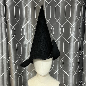 May include: A black pointed witch hat with a wide brim. The hat is on a white mannequin head.